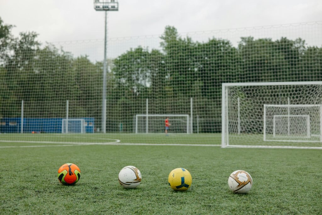 Four soccer balls on an outdoor field near goalposts, ideal for sports themes.